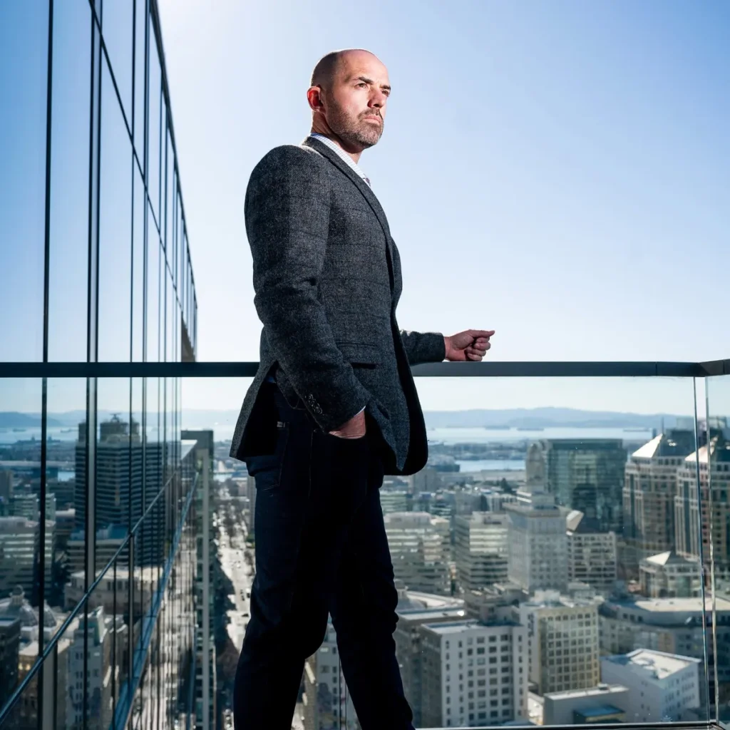 Colin Behring, CEO of Behring Companies, standing on a balcony overlooking downtown Oakland with the city skyline and Bay in the background.