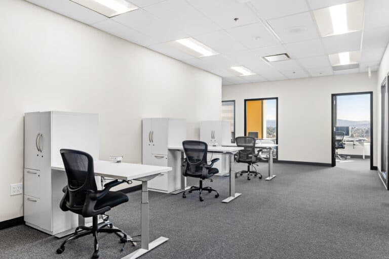 Open office with cubicles, desks, task chairs, and large windows.