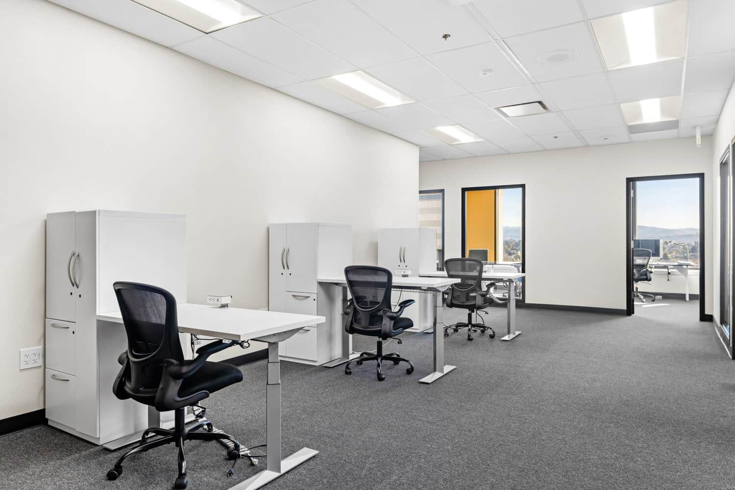 Open office with cubicles, desks, task chairs, and large windows.