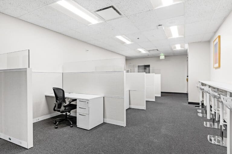 Open office with white cubicles, task chairs, and fluorescent ceiling lights.