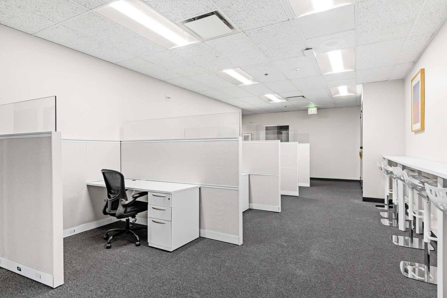 Open office with white cubicles, task chairs, and fluorescent ceiling lights.