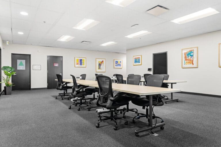 Open office with shared tables, task chairs, wall art, and white ceiling lights.