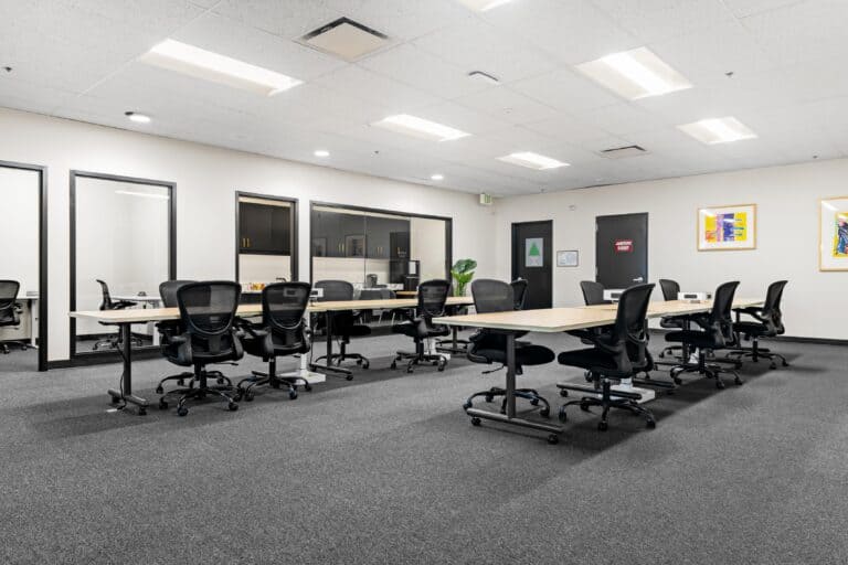Open office with shared tables, task chairs, and glass-fronted rooms.