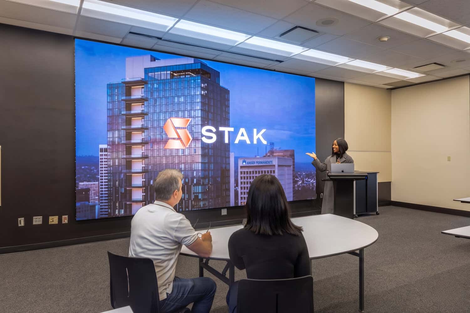 Small group seated in a presentation room facing a large STAK screen.