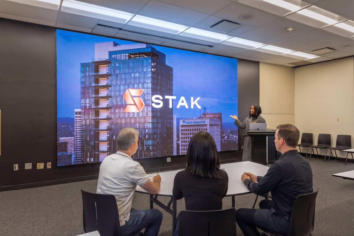 Small group seated in a presentation room facing a STAK screen.