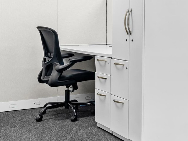 Simple desk setup with black task chair, white cabinets, and drawers.