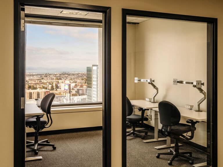 Private office with desks, chairs, and city view through large windows.