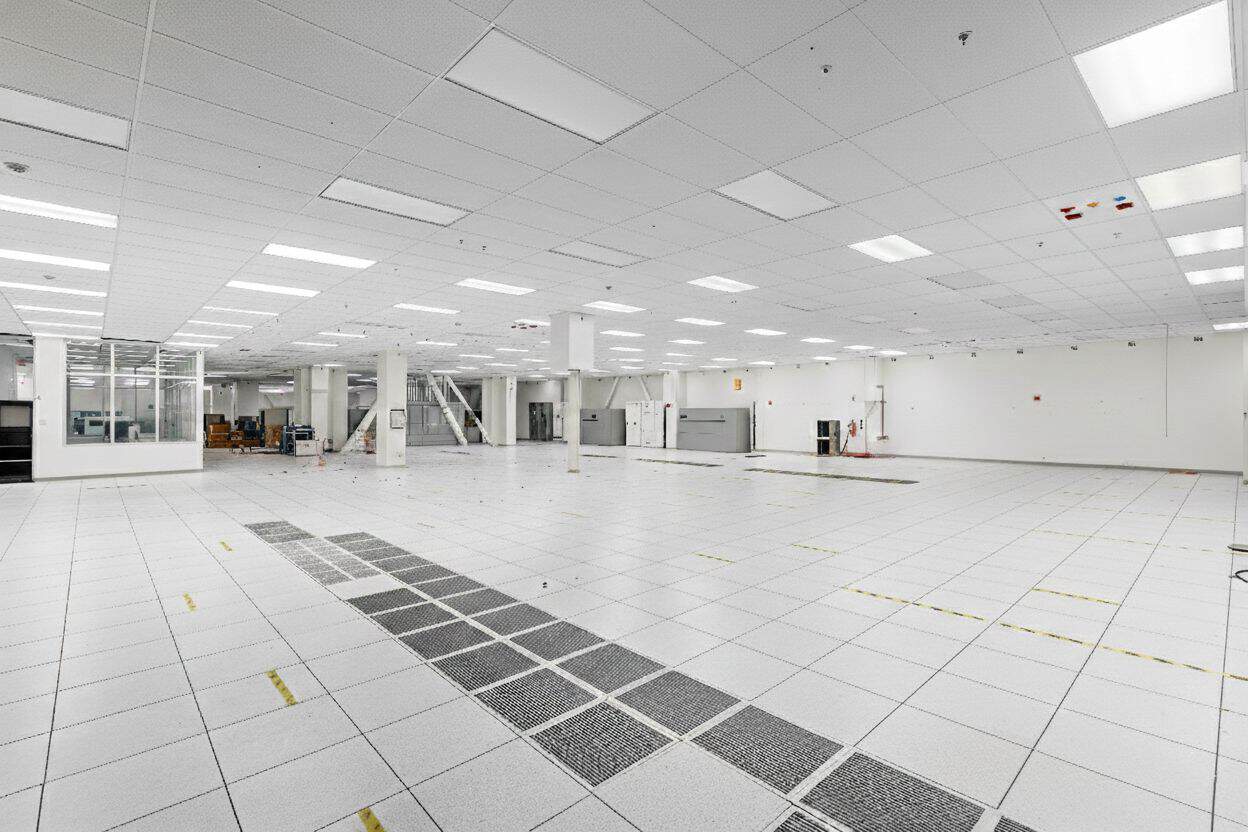 Large white data center room with overhead lighting and floor utility panels.